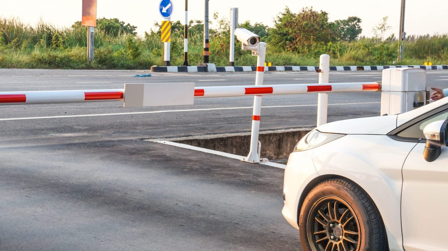 A white car parked at a barrier which has a camera to identify license plates
