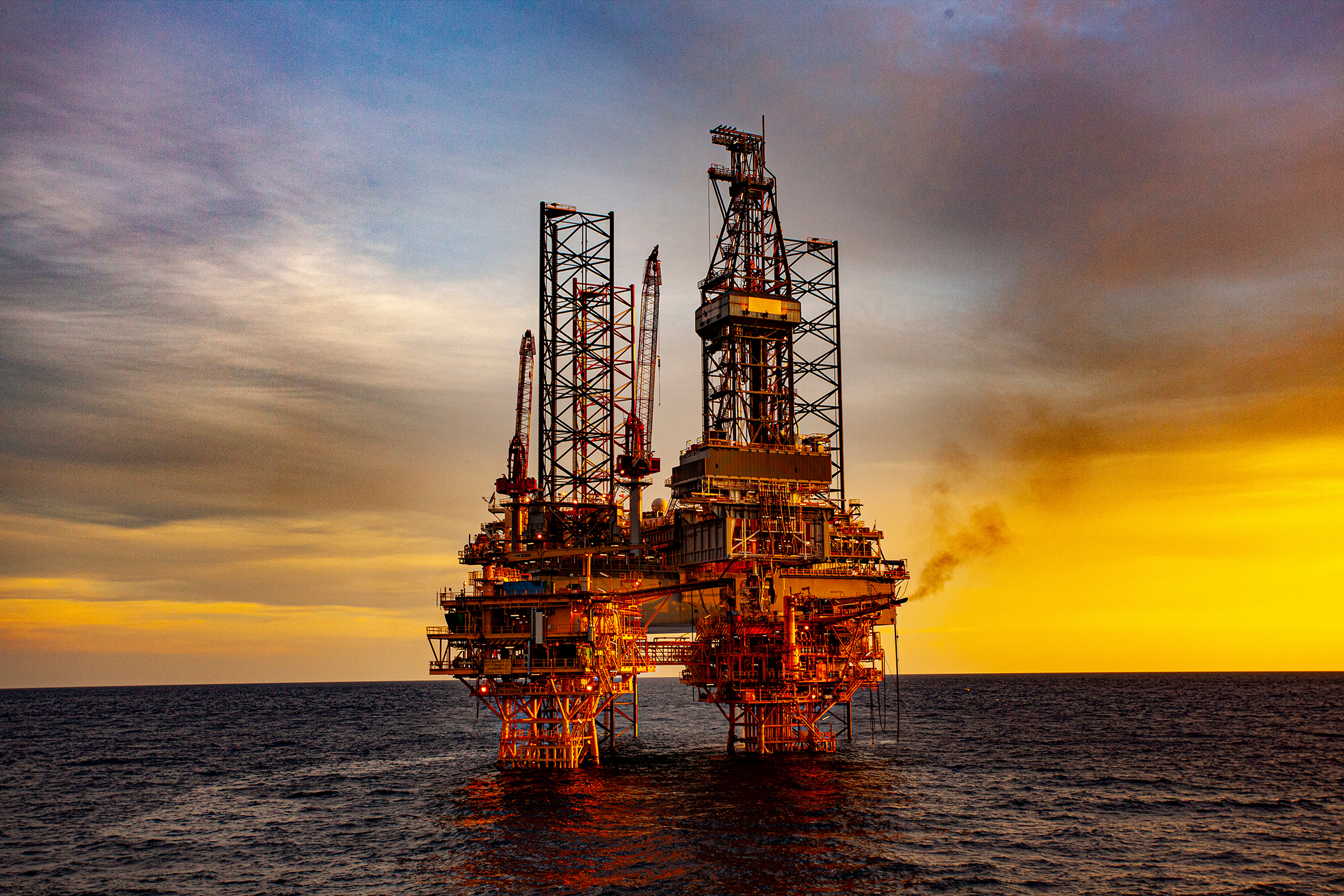 an oil rig surrounded by the ocean and a sunset